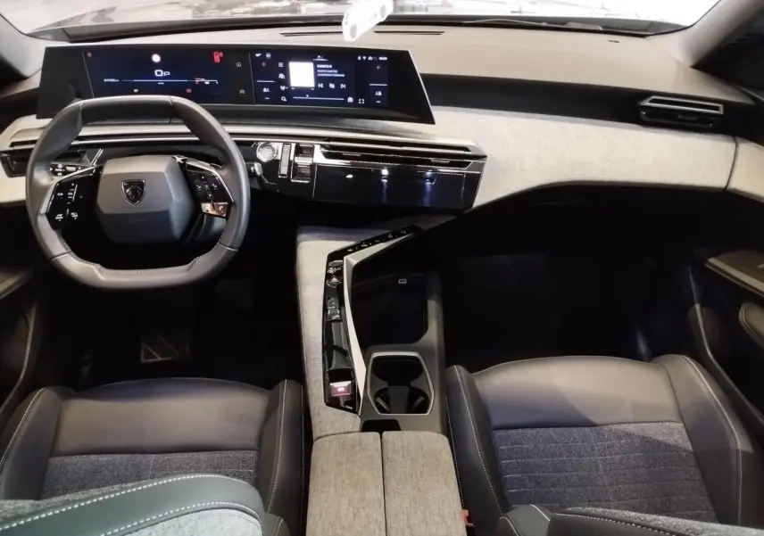 Intérieur Peugeot 5008 2025 vu de face, tableau de bord moderne avec double écran et sellerie tissu gris et cuir noir.