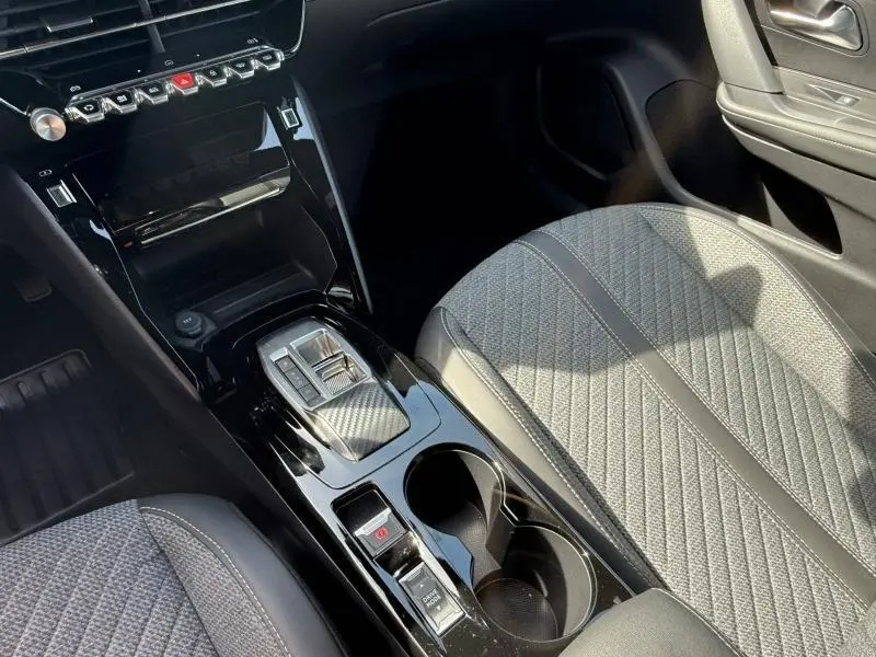 Vue intérieure centrée sur la console centrale et siège passager tissu gris du Peugeot 2008 hybride 2025.