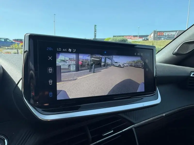 Écran tactile intérieur du Peugeot 2008 2025 montrant la caméra de recul avec vue sur un véhicule rouge Elixir à l'extérieur.