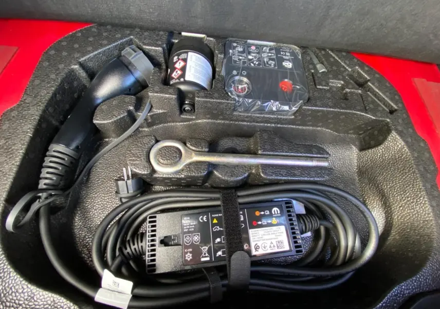 Gros plan sur le compartiment de rangement rouge du FIAT 500 Cabriolet Electrique avec câble de recharge et outils.