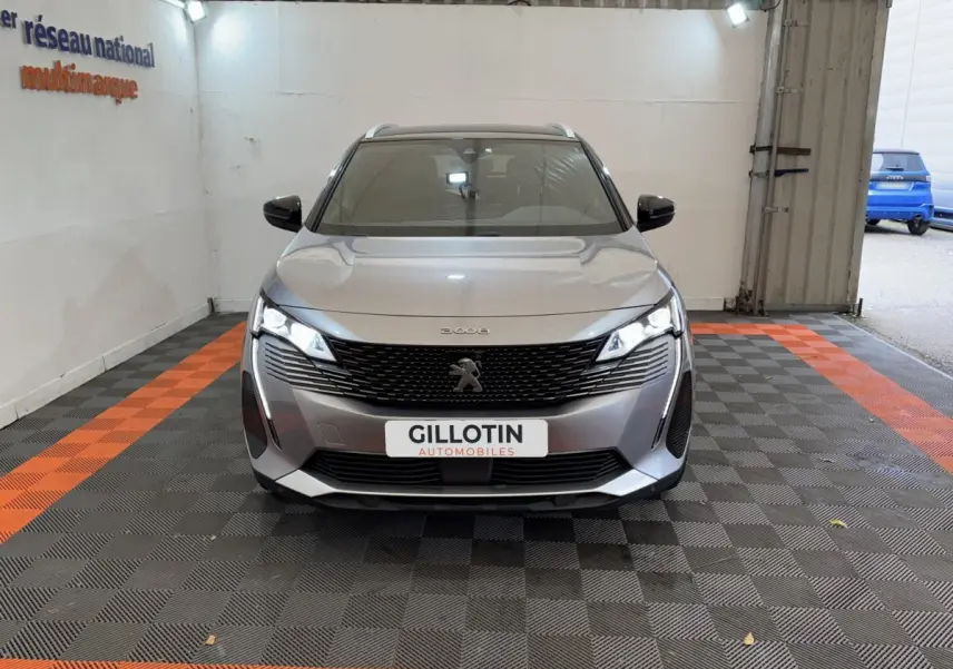 Vue avant d'un Peugeot 3008 gris clair avec calandre noire et phares LED allumés dans un garage.
