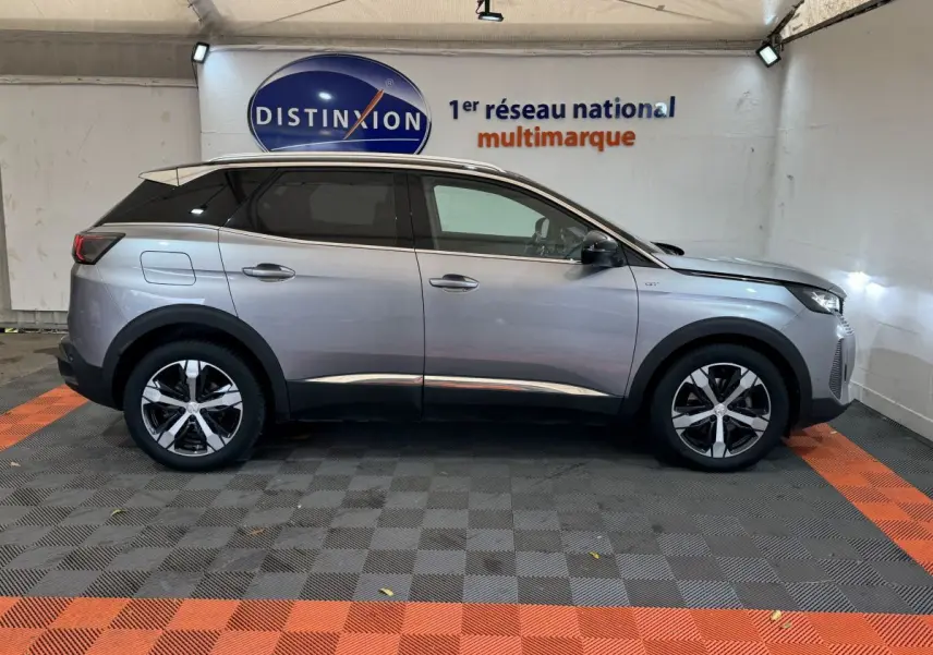 Profil droit d’un Peugeot 3008 GT gris clair 2021, avec jantes alliage et toit noir dans un garage.