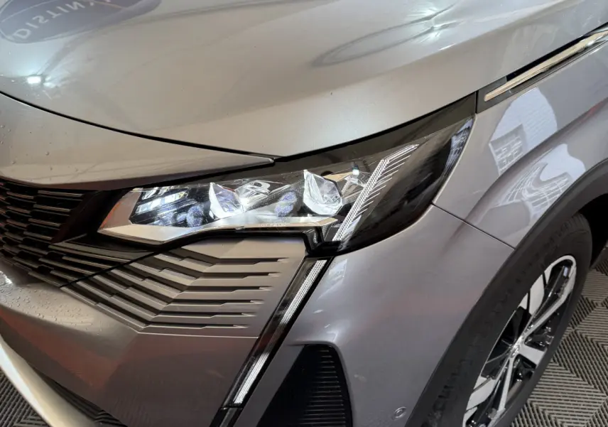 Gros plan sur l'avant droit gris clair du Peugeot 3008 2021, mettant en valeur le phare LED et la calandre distinctive.