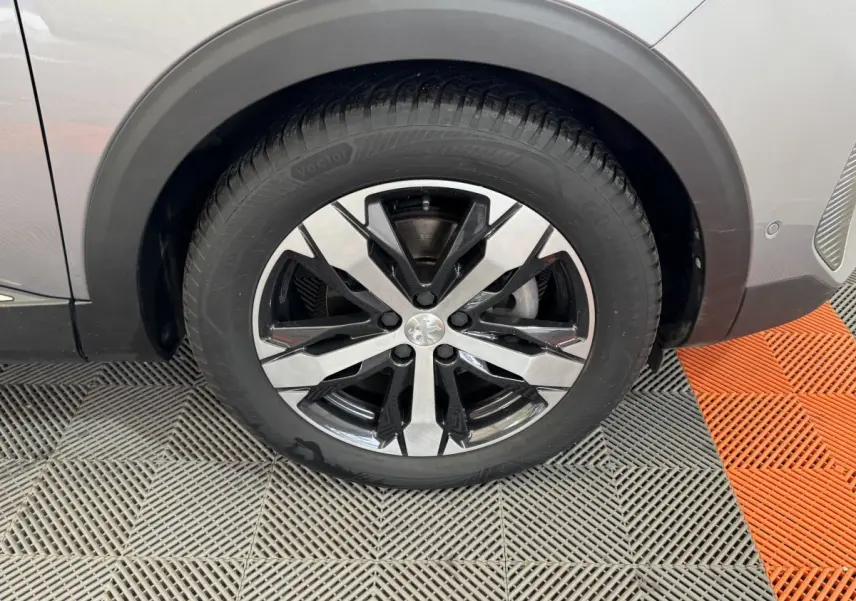 Gros plan sur la roue avant droite du Peugeot 3008 gris clair, mettant en valeur la jante alliage bicolore moderne.