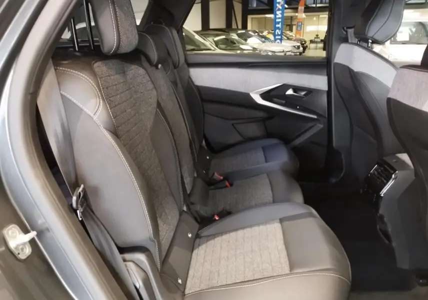 Vue latérale des sièges arrière en tissu gris et cuir sur Peugeot 5008 gris titanium, avec porte et console centrale visibles.