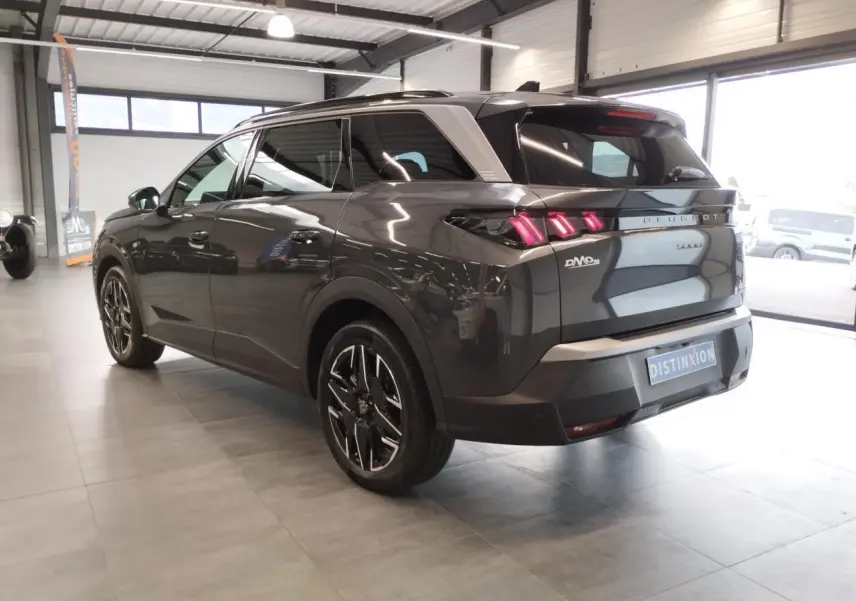 Vue 3/4 arrière droit d'un Peugeot 5008 gris titanium avec jantes alliage noires et feux arrière LED en griffes dans un showroom.