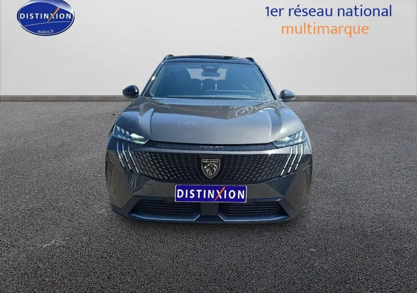 Vue frontale d'un Peugeot 5008 gris titane avec calandre noire et phares LED allumés sur sol goudronné.