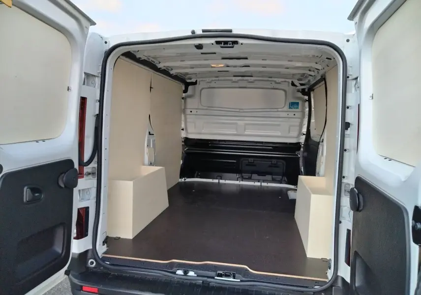 Vue arrière ouverte du Nissan Primastar blanc 2025 avec aménagement bois intérieur et plancher noir.