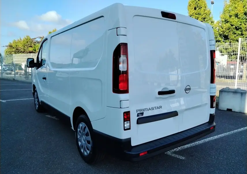 Vue 3/4 arrière droite d'un utilitaire Nissan Primastar blanc avec logo et marquage visible sur porte arrière.