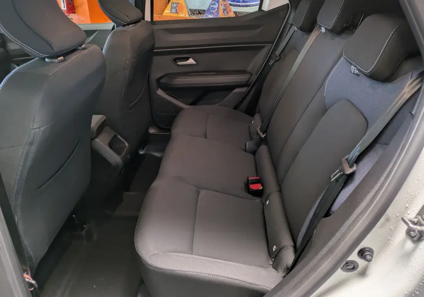 Vue intérieure côté droit des sièges arrière noirs du Dacia Duster Hybrid 140 Journey blanc glacier 2025, avec ceinture de sécurité visible.