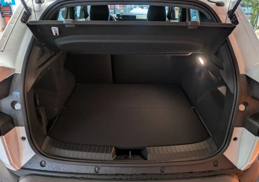 Coffre ouvert vu de l'arrière d'un Dacia Duster blanc glacier, montrant un espace de chargement propre et éclairé.