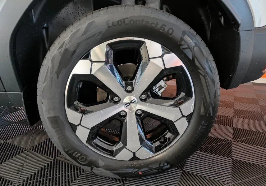 Gros plan sur la roue arrière droite du Dacia Duster blanc glacier, mettant en valeur la jante alliage 18 pouces et le passage de roue noir.