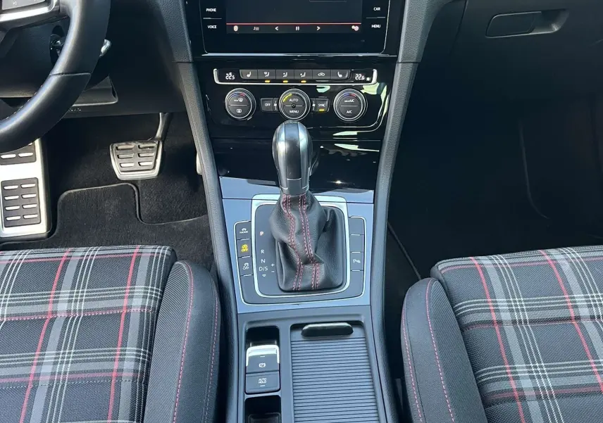 Vue intérieure centrée sur la console centrale et la boîte automatique d'une Volkswagen Golf GTI Performance avec sièges à motif tartan.