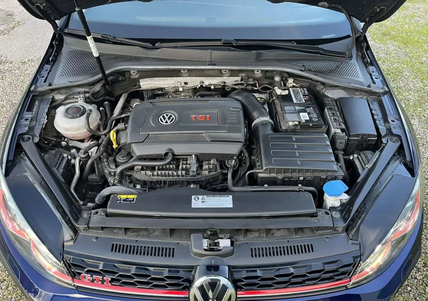 Vue plongeante sur le moteur TSI d'une Volkswagen Golf VII GTI Performance bleu lapiz, capot ouvert et logo GTI visible.