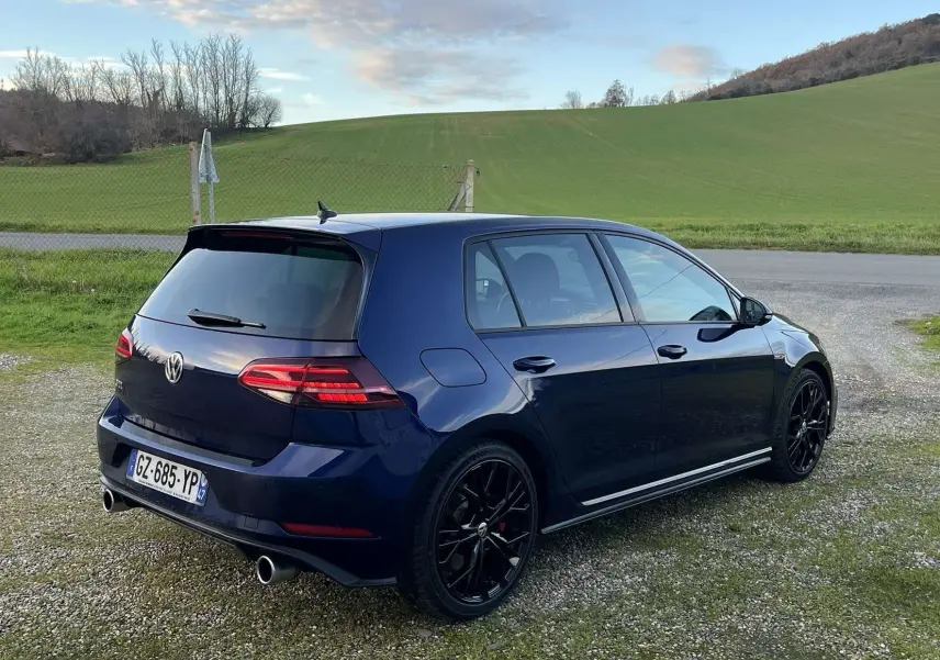 Volkswagen Golf VII GTI Performance bleu Lapis Metal vue 3/4 arrière droit avec jantes noires et double sortie d’échappement.