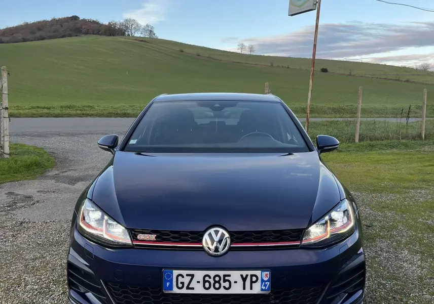 Vue de face d'une Volkswagen Golf VII GTI Performance bleu lapiz metal avec calandre noire et bande rouge distinctive.