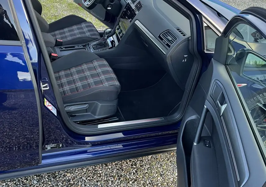 Intérieur côté conducteur d'une Volkswagen Golf VII bleu lapiz, sièges à motif tartan et tableau de bord moderne.