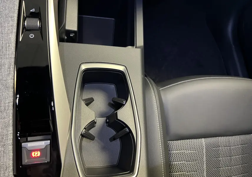 Gros plan sur la console centrale noire et porte-gobelets, avec siège avant en cuir noir partiellement visible à droite