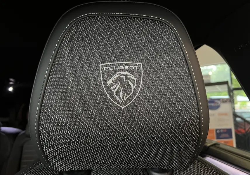 Gros plan sur l'appui-tête noir brodé du lion Peugeot à l'intérieur du SUV 5008 hybride 2025.