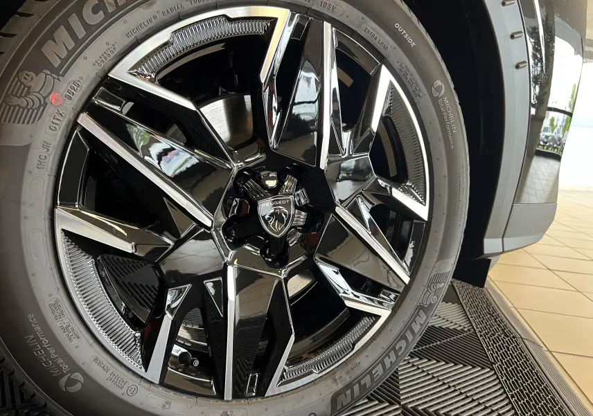 Gros plan sur la jante alliage 19’’ noire et brillante du Peugeot 5008 NV HYBRID 136 E-DCS6 GT noir, avec pneu Michelin visible.
