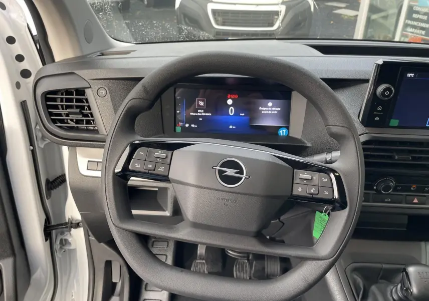Vue rapprochée du volant noir et du tableau de bord numérique de l'Opel Vivaro blanc 2024 avec boîte manuelle.