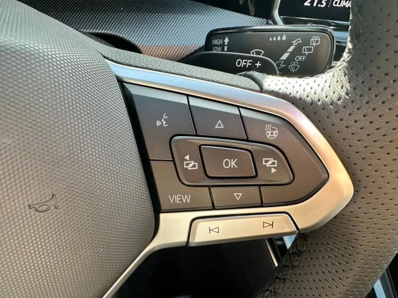 Gros plan sur les commandes au volant côté gauche d’une Volkswagen Golf gris 2025, avec boutons multifonctions et volant perforé.