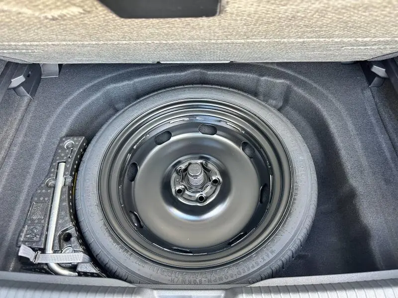 Roue de secours noire dans le coffre d'une Volkswagen Golf 1.5 eTSI R-Line Edition 2025, avec outil de levage visible.