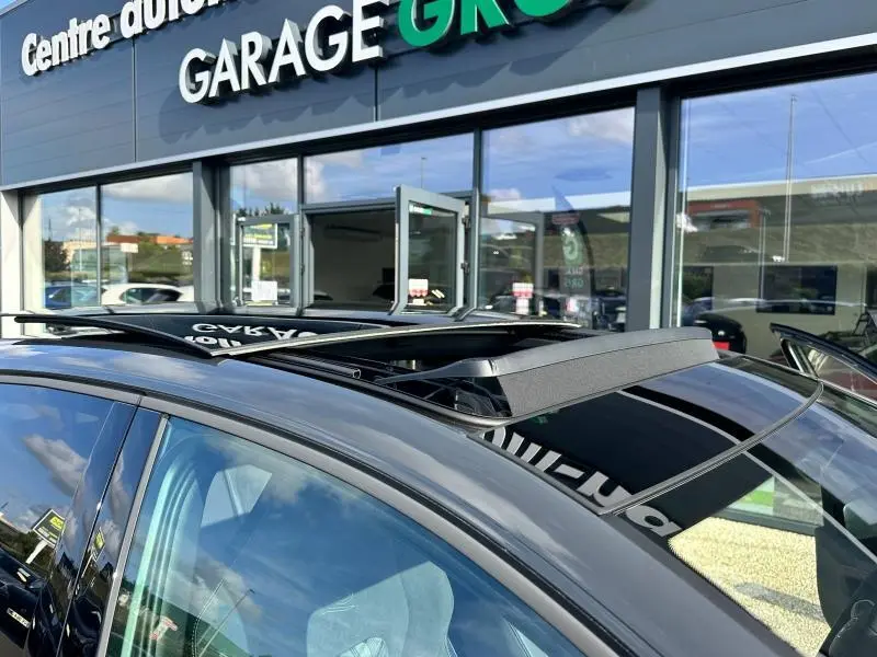 Toit ouvrant ouvert sur le côté gauche d'une Volkswagen Golf gris 2025 R-Line devant un garage.