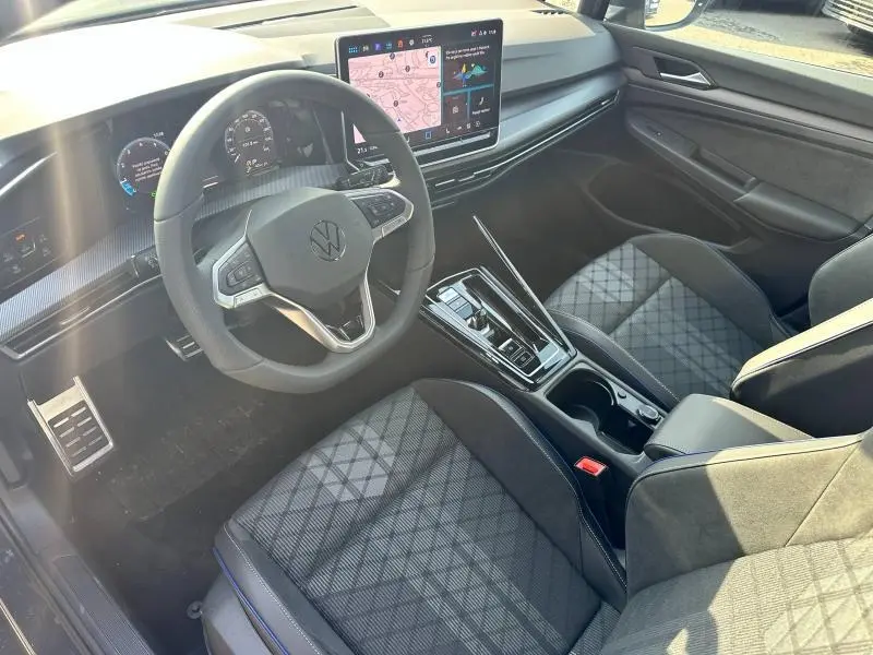 Vue intérieure côté conducteur de la Volkswagen Golf 1.5 eTSI R-Line 2025 avec sièges tissu gris et écran tactile central.
