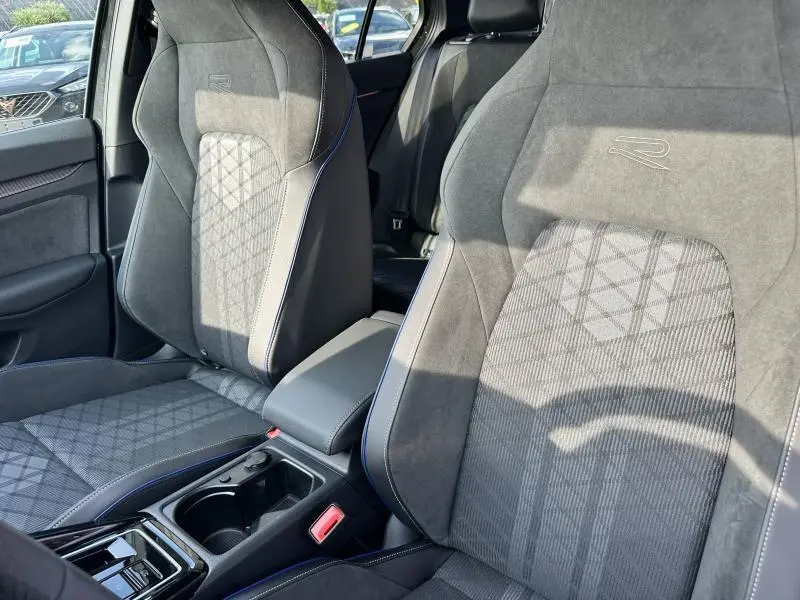 Vue rapprochée des sièges avant gris de la Volkswagen Golf 1.5 eTSI R-Line Edition 2025 avec logo "R" brodé et surpiqûres bleues.