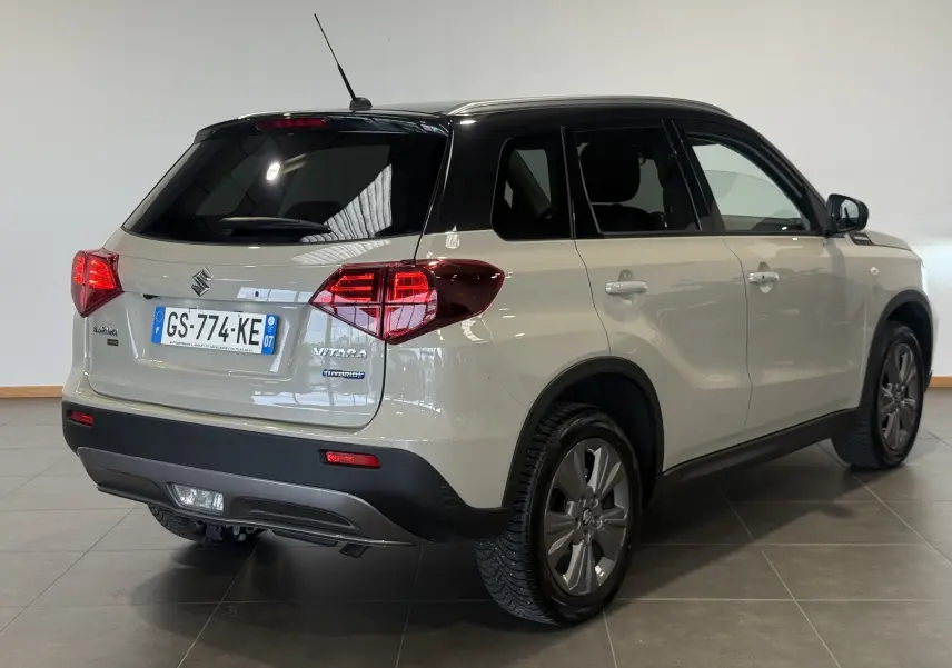 Vue 3/4 arrière droite du Suzuki Vitara beige 2023 avec toit noir et badges Hybrid et Allgrip visibles.