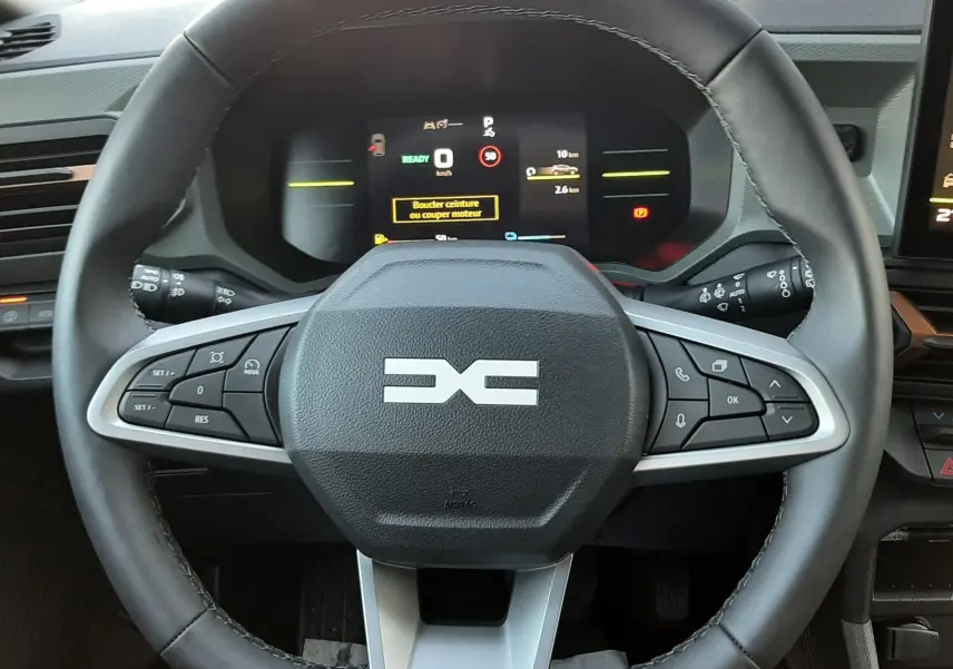 Volant noir avec logo DACIA stylisé, tableau de bord numérique et commandes intégrées, intérieur du Dacia Duster 2025.