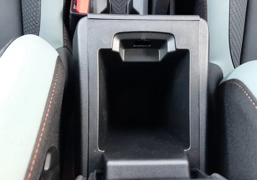 Vue plongeante sur le rangement central ouvert entre les sièges gris clair et noir du Dacia Duster Sandstone 2025.