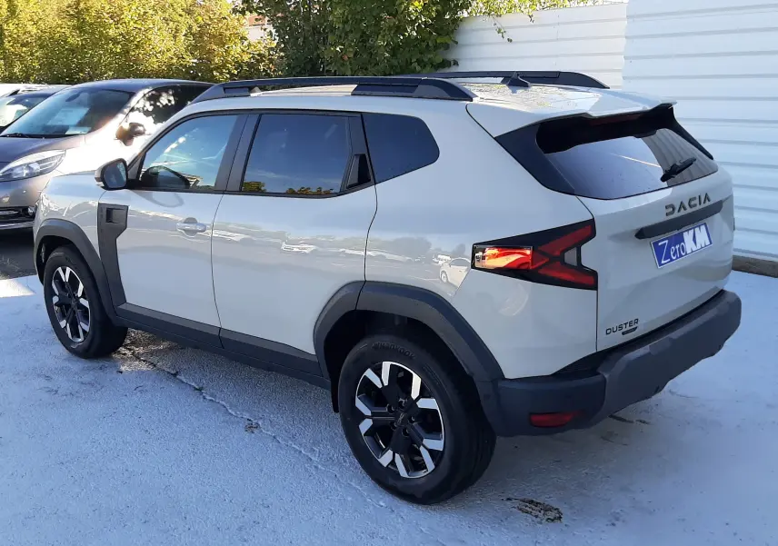 Vue 3/4 arrière droite du Dacia Duster 2025 couleur Sandstone avec jantes biton et feux arrière allumés.