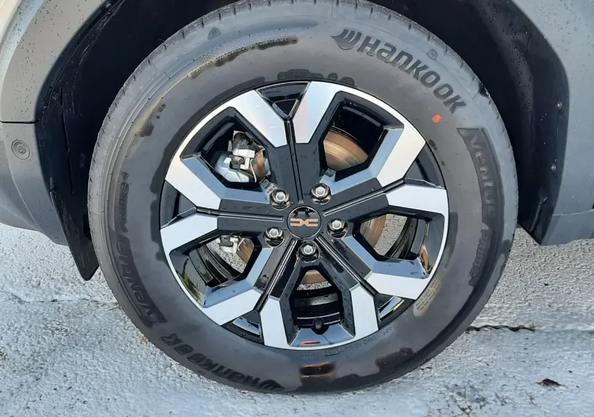 Gros plan sur la roue avant droite du Dacia Duster 1.6 Hybrid 140ch Extreme en couleur Sandstone, jante alliage noire et argent.