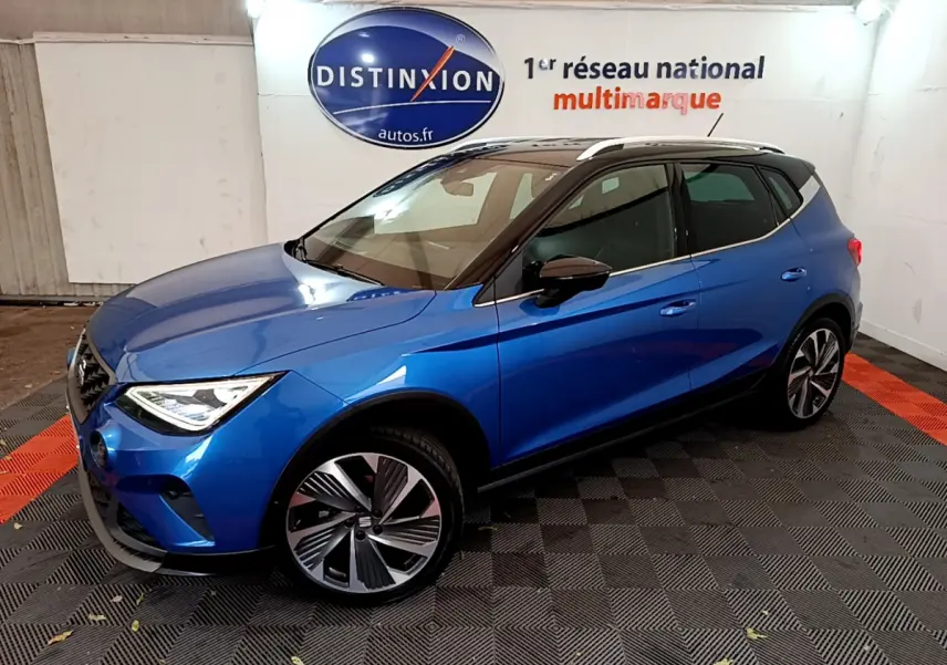 SEAT Arona bleu en 3/4 avant droit, toit noir et jantes alliage distinctives dans un showroom intérieur.