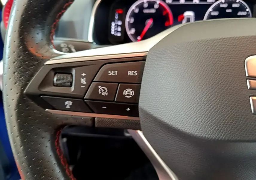 Gros plan sur le volant cuir avec commandes multifonctions à gauche du SEAT Arona bleu 2022, tableau de bord en arrière-plan.