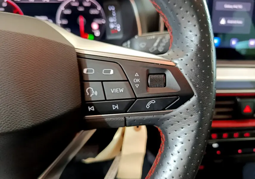 Gros plan sur le côté droit du volant cuir perforé avec surpiqûres rouges du SEAT Arona 2022, commandes multifonctions visibles.