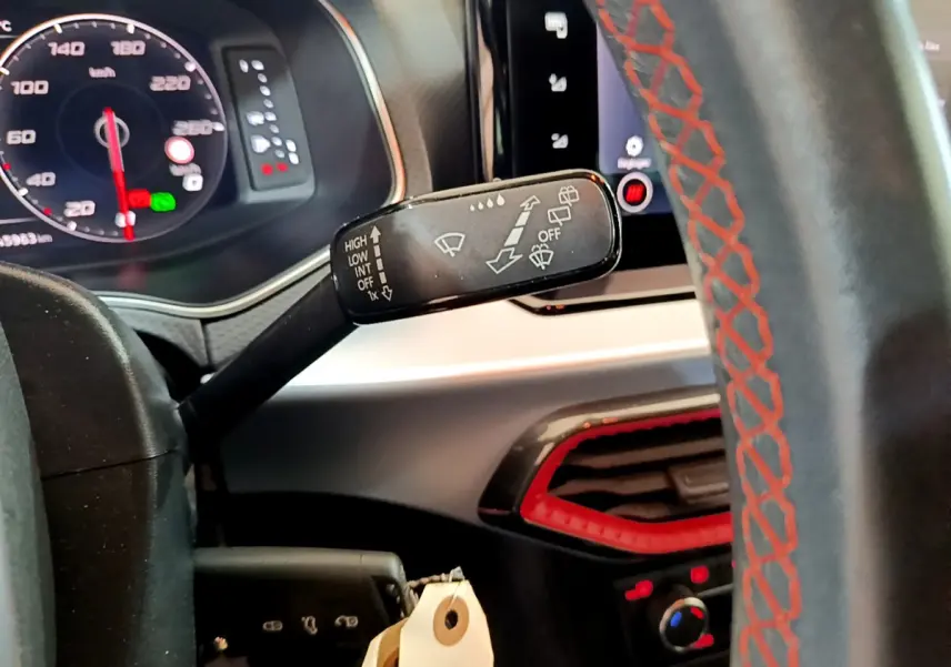 Gros plan sur le commodo d'essuie-glace et le volant avec surpiqûres rouges dans l'habitacle du SEAT Arona bleu 2022.