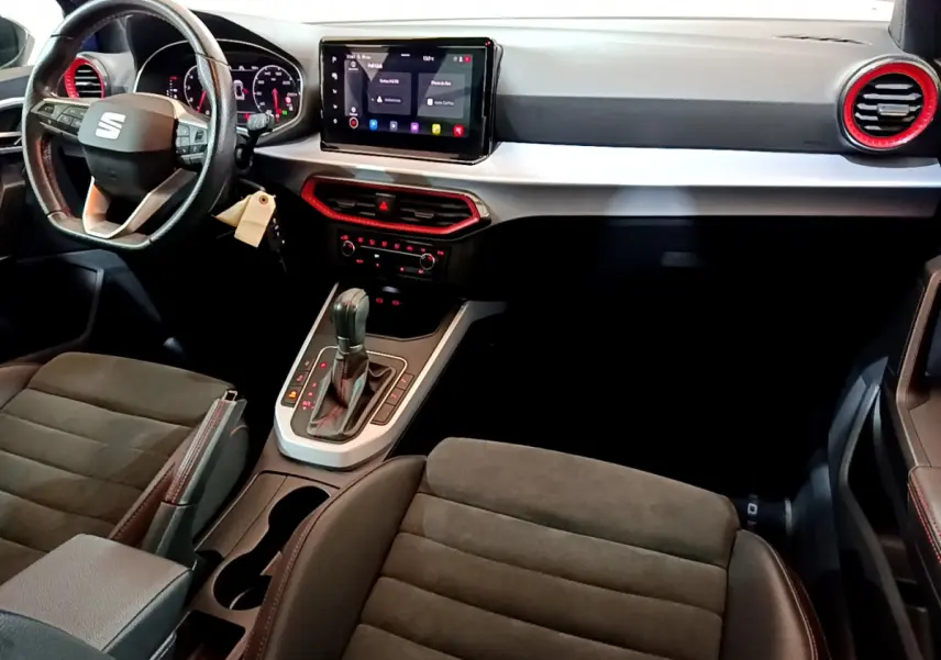 Intérieur du SEAT Arona 2022 vu côté conducteur, tableau de bord noir avec touches rouges et écran tactile central.