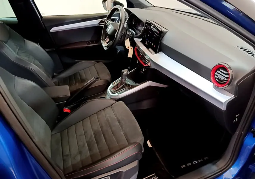 Intérieur côté conducteur d'une SEAT Arona bleu 2022, avec tableau de bord moderne et sièges noirs à surpiqûres rouges.