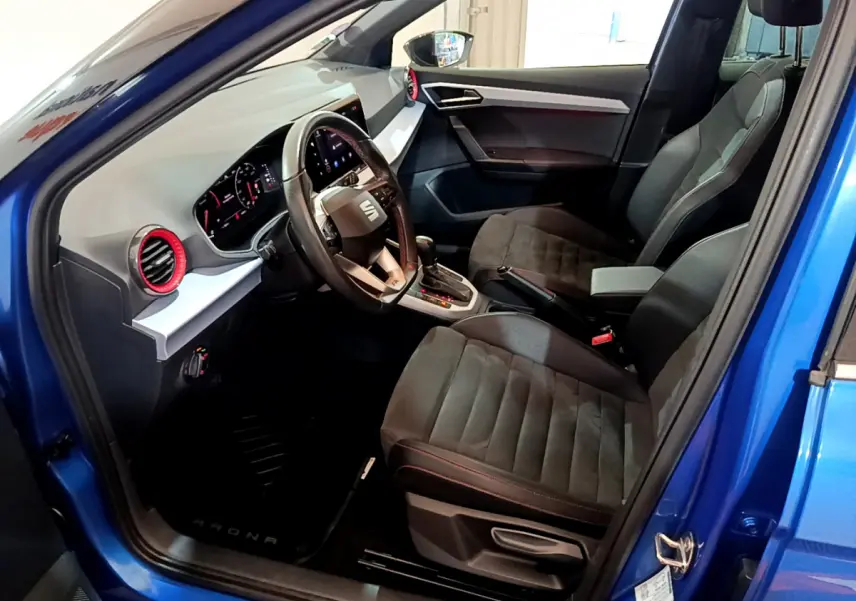 Intérieur côté conducteur d'une SEAT Arona bleu 2022, montrant sièges noirs et tableau de bord moderne avec volant cuir.