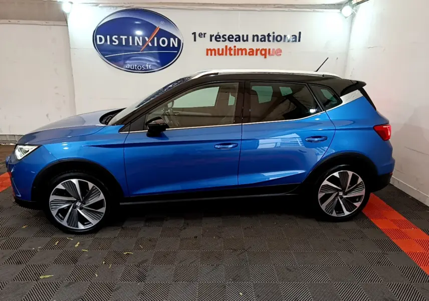 Profil côté gauche d'un SEAT Arona bleu 2022 avec toit noir et jantes alliage stylisées en intérieur showroom.