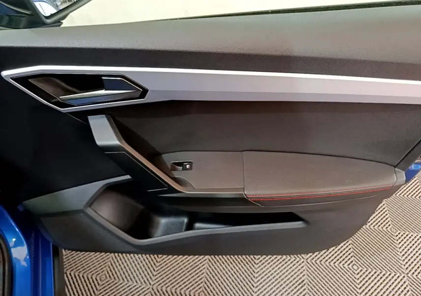 Porte intérieure côté gauche de la SEAT Arona bleu 2022 avec surpiqûres rouges et poignée argentée.
