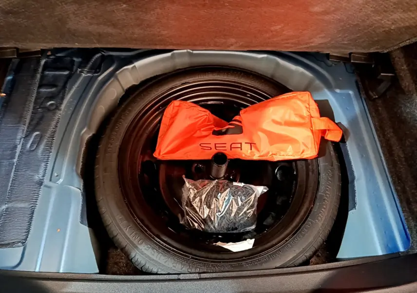 Vue plongeante sur la roue de secours noire dans le coffre bleu du SEAT Arona avec un sac orange marqué SEAT.