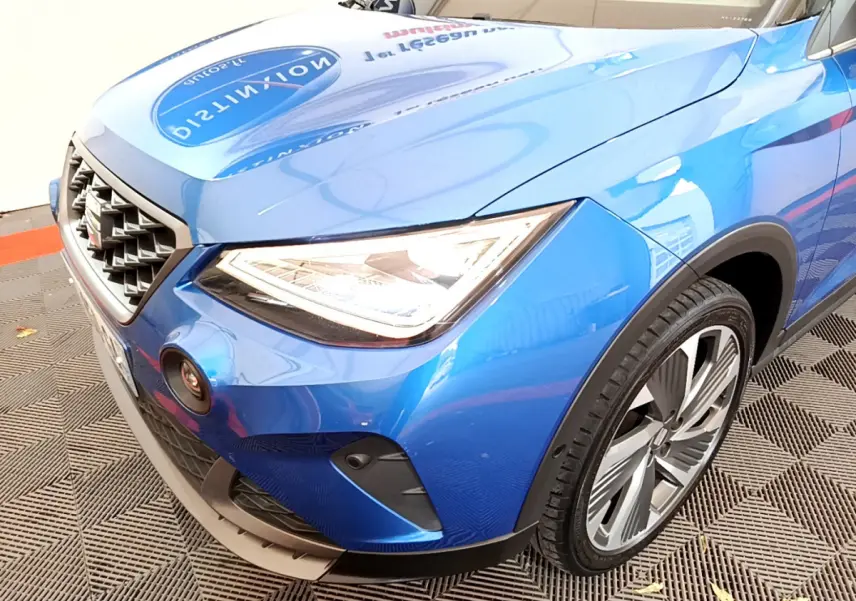 Vue 3/4 avant droit d'une SEAT ARONA bleu brillant mettant en valeur son phare LED et sa calandre distinctive.