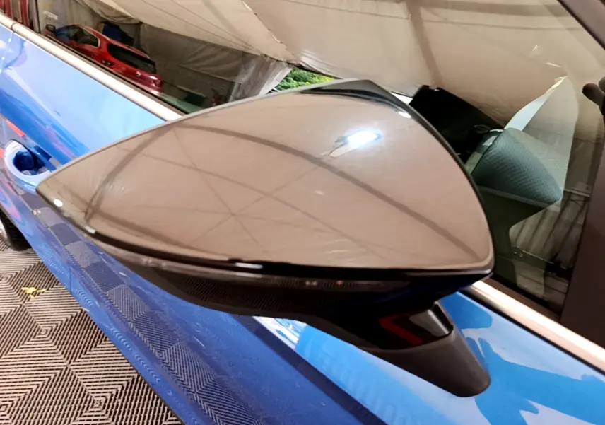 Rétroviseur côté gauche noir brillant sur SEAT Arona bleu, avec reflet de la tente et intérieur visible.