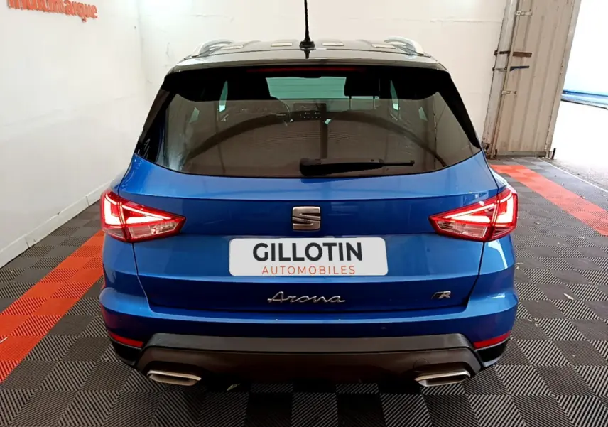 Vue arrière d'un SEAT Arona bleu 2022 finition FR avec feux LED et double sortie d'échappement dans un garage.