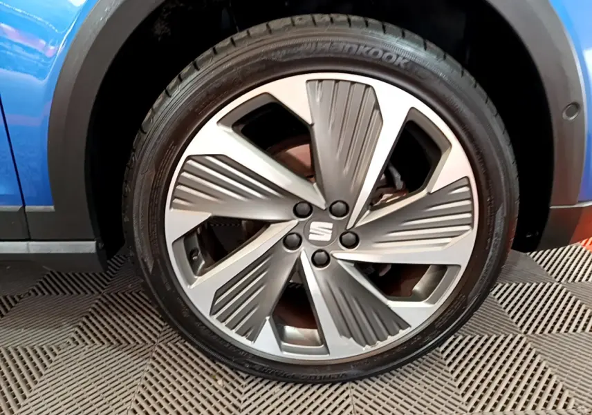 Gros plan sur la jante alu argentée du côté avant gauche d'une SEAT Arona bleue 2022, avec logo central visible.