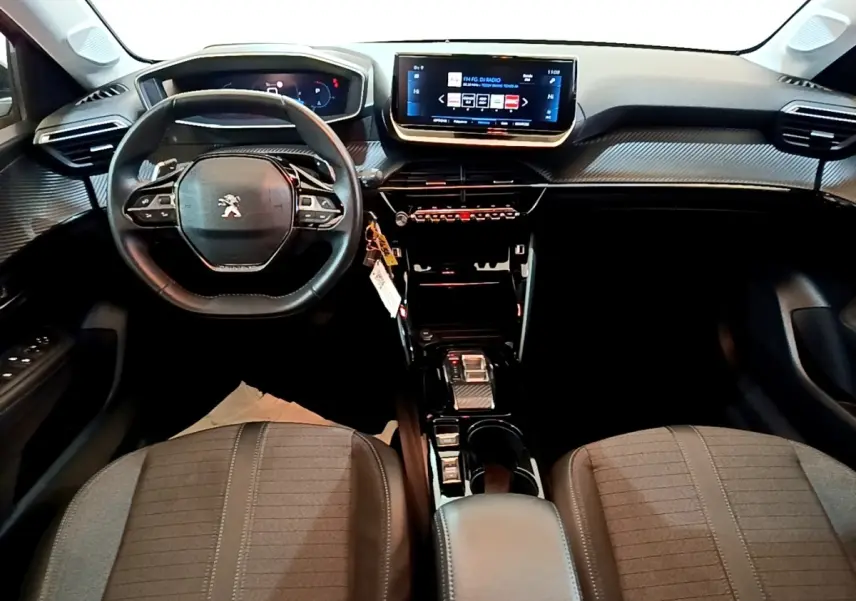 Vue intérieure avant de la Peugeot 208 2023, tableau de bord moderne avec écran tactile central et volant multifonctions cuir.